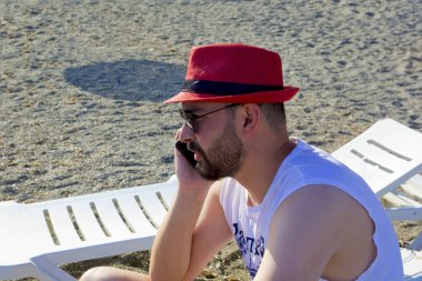 Kumsalda kırmızı şapkalı yakışıklı genç adam.