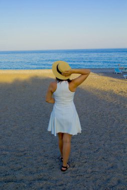 Güzel genç bir kadın sahilde duruyor.