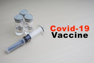 COVID - 19 VACCINE metni, üzerinde şırınga ve ahşap kaplama şişeleri var. Coronavirus veya Covid-19 Aşı Konsepti