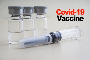COVID - 19 VACCINE metni, üzerinde şırınga ve ahşap kaplama şişeleri var. Coronavirus veya Covid-19 Aşı Konsepti