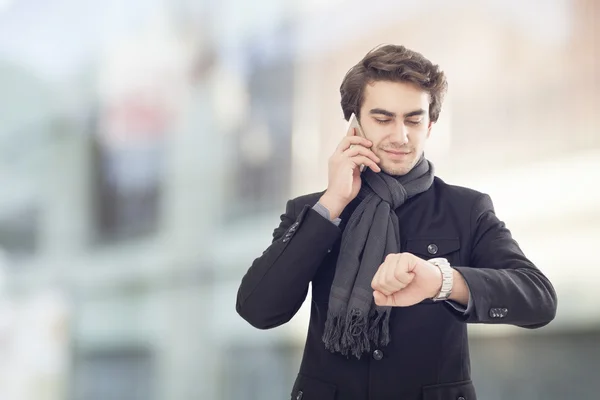 Junger Geschäftsmann telefoniert mit dem Handy und schaut auf die Uhr auf der Straße — Stockfoto