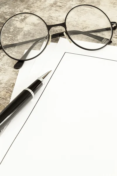 Blank paper, pen and glasses on wooden table