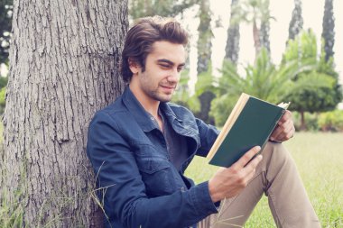 Genç adam parkta kitap okuyor.