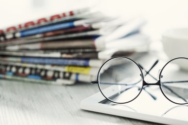 Gazeteler, gözlük ve dijital tablet yığını