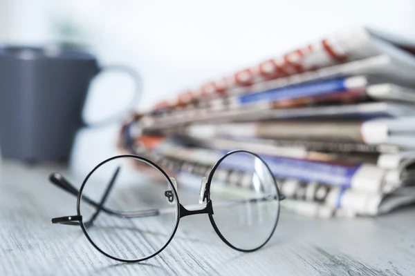 Stack of newspapers, eyeglasses on table — Stock Photo, Image