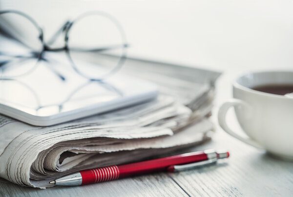 Stack of newspapers, eyeglasses and digital tablet