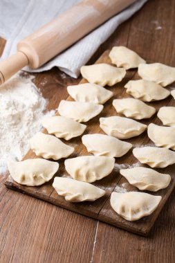 Hamur tatlısı, vareniki, pierogi, ahşap tahtada merdane iğnesiyle un serpiştirme işlemi. Geleneksel Ukrayna yemeklerine yakından bak. Seçici odak.