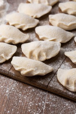 Tahta tahtaya un serpiştirilmiş hamur tatlısı, vareniki, pierogi yapma süreci. Çiğ yarı pişmiş yemek. Geleneksel Ukrayna yemeklerine yakından bak. Seçici odak.