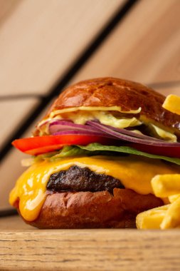 Tahta arka planda izole edilmiş patates kızartmalı büyük bir çizburger. Hamburger, köfteli soğan, domates, marul turşusu, erimiş çedar, hardal, domates reçeli, mayonez. Yatay