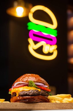 Arka planda neon burgerli patates kızartmalı Big Cheeseburger. Hamburger köfteli soğan, domates, marul turşusu, erimiş çedar, hardal, domates reçeli, mayonez..