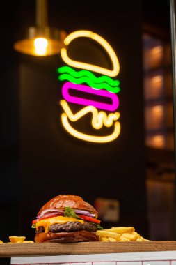 Arka planda neon burgerli patates kızartmalı Big Cheeseburger. Hamburger köfteli soğan, domates, marul turşusu, erimiş çedar, hardal, domates reçeli, mayonez..