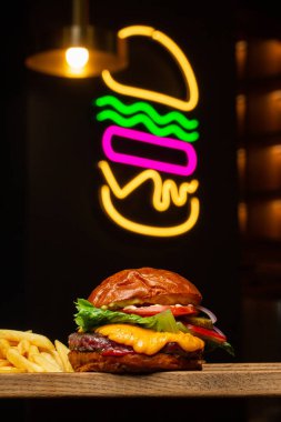 Arka planda neon burgerli patates kızartmalı Big Cheeseburger. Hamburger köfteli soğan, domates, marul turşusu, erimiş çedar, hardal, domates reçeli, mayonez..