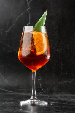Portakal ve fesleğen yaprağı dilimleriyle süslenmiş şarap kadehinde servis edilen bir bardak soğuk Aperol spritz kokteyli.