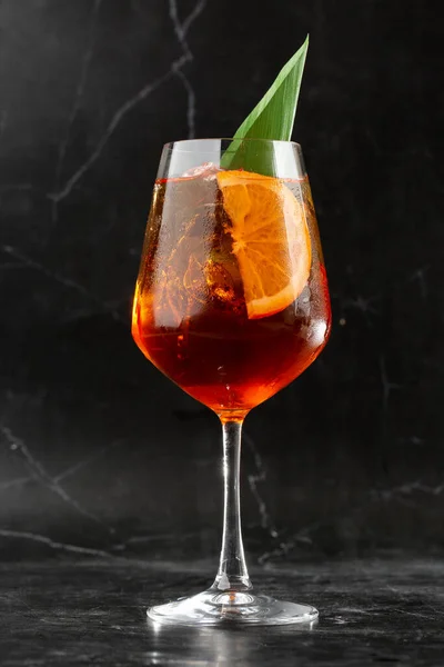Portakal ve fesleğen yaprağı dilimleriyle süslenmiş şarap kadehinde servis edilen bir bardak soğuk Aperol spritz kokteyli.