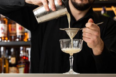 Profesyonel barmen elek kullanarak bardaktan bardağa portakal alkollü kokteyl döker. Bulanık görünüm.