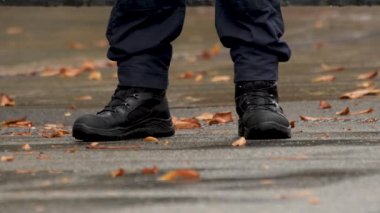 Sonbahar. Ayrıntılar. Askerî botlar erkek ayağında. Polis ayakları işte. Üniformalı polis memurunun botları. Bir polisin bacakları görev başında. Siyah çizmeli güvenlik görevlisi. Düşen Yapraklar