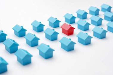 Kırmızı minyatür ev modeli, aynı tip minyatür evlerden farklı olarak üç sıra halinde dizilmiş mavi oyuncak evler arasında. Kır köyünde emlak ve emlak pazarı. İpotek ve ev satın alma