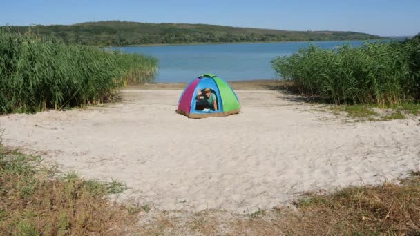 Positive Mann lächelt freundlich und zeigt Hallo Hand oder Hallo und guten Morgen Eröffnung Zelt camping. Mann winkt grüßende Hand im Touristenzelt oder Daumen-hoch-Geste am Fluss oder See bei Öko-Reisen — Stockvideo