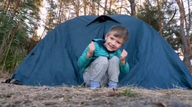 Mutlu çocuk gülümsüyor, komik dans ediyor ya da çocukla birlikte çevrede gezintiye çıkıyor. Olumlu çocuk yeşil çadırın yanında eğleniyor. Ormanda aktif bir hafta sonu geçirmenin tadını çıkarıyor.