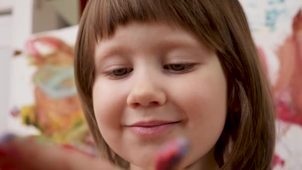アーティストの赤ん坊の女の子は彼女の手の子供の芸術療法をペイントする。カラフルな絵画の子供たちに手を描く創造的な子供の顔をクローズアップ子供は色を学ぶヤシの幼児感覚プレイアート開発ゲーム幸せな赤ちゃん — ストック動画