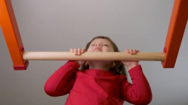 Bardaki çocuk spor salonu barında. Küçük kız barfiks çekiyor ya da çene yukarı kalkıyor. Küçük kız spor salonundaki spor salonunda kendini yukarı çekiyor çocuklar.
