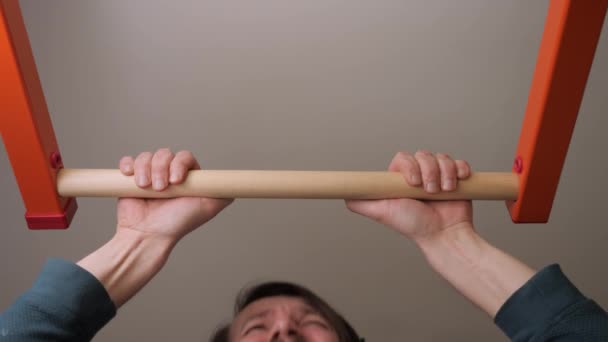 Hombre motivado haciendo tirando hacia arriba en la barra horizontal en casa gimnasio esfuerzo cara ejercicio deportivo barbilla hacia arriba. Ejercicio pull-ups. Quiere ser fuerte chico débil intenta empujado hacia arriba en la barra de gimnasia entrenamiento hombre esfuerzo cara — Vídeo de stock