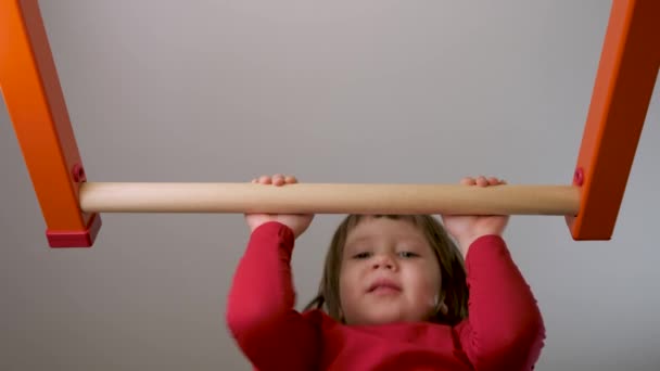 Développement physique enfants éducation sportive. Entraînement d'enfant à la maison en forme. Le gosse fort tire vers le haut exercice de barre sur la barre gymnastique. Petite fille exercice menton jusqu'à la barre d'entraînement enfant sur barre horizontale gymnase enfant athlète — Video