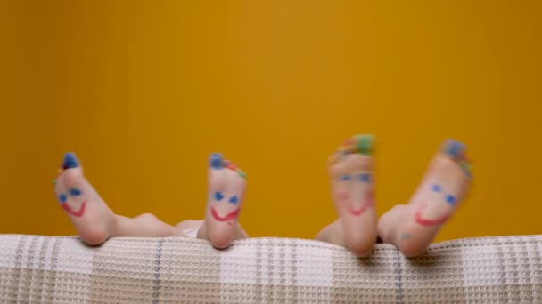 Краска забавные ноги детей с улыбкой рисования пальцев ног. Босоногий ребенок играет и танцует пальцами на ногах красочные смешные детишки ног. Раскрашенные счастливые улыбки детей ноги в постели размахивая смешной концепцией ноги на желтом фоне — стоковое видео
