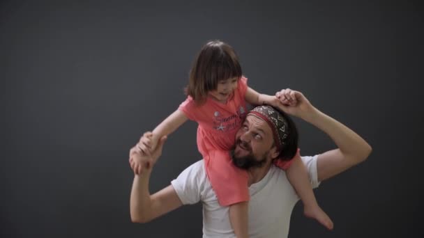 Piggyback rijden op papa. Glimlachende dochter heeft plezier in de nek vader spinning kind houdt zijn vader schouders. Jonge vader gooit zijn dochter terug op papa. Fijne vaderdag. Rommel met papa. — Stockvideo