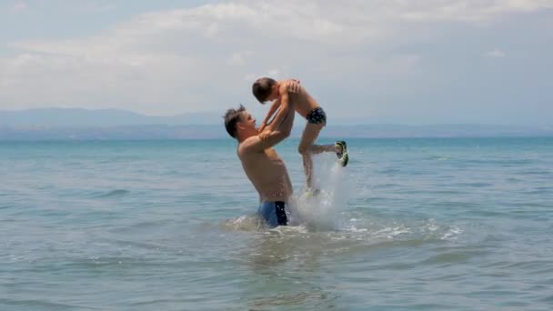 Tata z aktywnością dzieci letnie wakacje na plaży. Morze wakacje lato wolność wody zabawa. Ojciec wrzuca syna do wody. Ojciec i dziecko bawią się w morzu pływając i bawiąc się w wodzie. Zwolniony ruch — Wideo stockowe