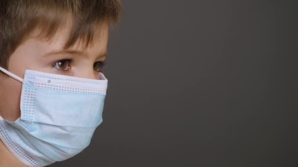 Close up kid in mask. Covid-19 child on gray background with copy space. Little boy wearing mask face on free space. Masked face child close up portrait boy in medical mask during coronavirus outbreak — Stock Video