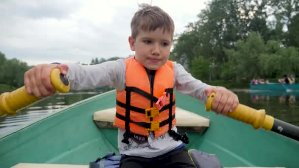 Pojke roddbåt barn. Grabben flyter på en båt flod semester. Grabben åker båt med paddel. Barnro åror på en båt en sjö park stad. Rekreationsläger för barn under semestrar på floden — Stockvideo