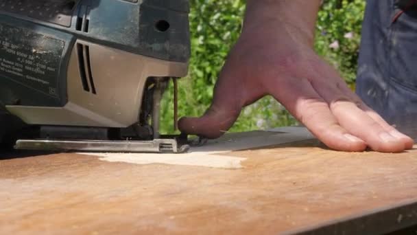 Primer plano del rompecabezas eléctrico en acción. Casa de reparación. Panel de madera de aserrado de carpintero. Herramientas de carpintería. El artesano corta la tabla con una sierra de calar. Joiner trabaja en una sierra eléctrica. Fabricación de muebles — Vídeos de Stock