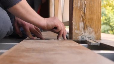 Evi onar. Döşeme terası. Marangoz tahta üzerine bir çizgi çekiyor. Köşedeki cetvelle döşeme tahtalarını kapatın. Ahşap tahtada kalem ve metre işaretleriyle birleştirici