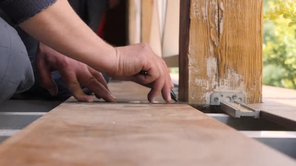 Επισκευή. Δάπεδο εγκατάσταση βεράντα. Ο ξυλουργός ζωγραφίζει μια γραμμή κοπής σε ξύλινη σανίδα. Κοντινό πλάνο μέτρησης σανίδων δαπέδου με γωνιακό χάρακα. Joiner με μολύβι και μετρητής μέτρησης σε ξύλινη σανίδα — Αρχείο Βίντεο