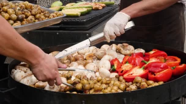 Grillowane warzywa. Jedzenie na świeżym powietrzu gotowanie pan smażone warzywa. Wegański posiłek. Dzwonnica smażona na dużej patelni z ziemniakami i grzybami. Pieczone warzywa grill gotowanie na ulicy żywności festiwalu — Wideo stockowe