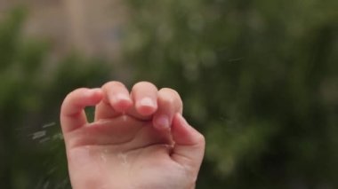 Yağmur damlaları çocuk eline düşer. Kötü hava koşulları pencerenin önünde yağmur altında çocuk suyu damlaları avuç içine düşen yağmur damlalarını yakalar. Yağmurlu bir hava var. Yağmurlu bir hava. Çocuklar elini bırakıyor.