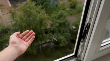 Erkek eline düşen yağmur damlaları doğaya dokunur. Pencereden yağan yağmurlu havada yağan el damlaları yakındır. Kötü hava pencerenin dışında, yağmur altında su damlaları. Avuç içlerine düşen yağmur damlaları