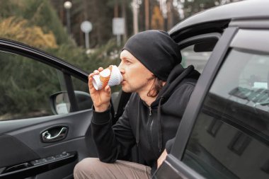 Erkek sürücü açık kapılı bir arabada otururken kahve içer. Kahve molası. dinlenirken yolda.