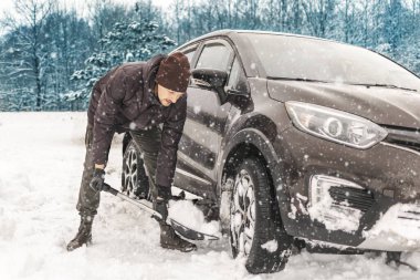 Adamın biri elinde kürekle şehrin dışında karda mahsur kalmış bir araba kazıyor. Karlı. Nakliye aracı, kara saplanmış bir araç. konsept.