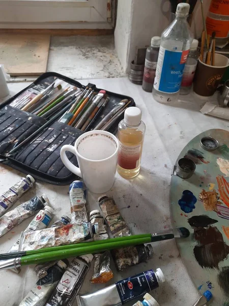 Boya fırçaları, sanatçı paleti, kalemler, kahve fincanı, suluboya ve resim stüdyosundaki yağlı boyalar.. — Stok fotoğraf