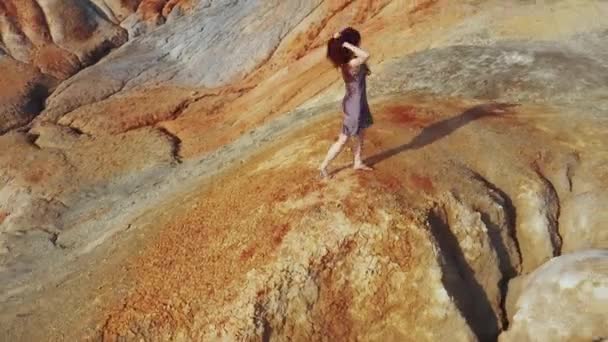 Вид с воздуха на девушку, которая поднимается на красные горы в платье — стоковое видео