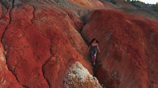 Luftaufnahme eines Mädchens, das in einem Kleid die roten Berge besteigt — Stockvideo