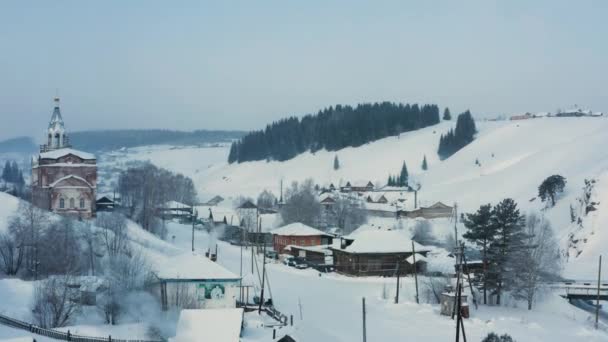 凍結した川のほとりの雪の中の村の空中風景 — ストック動画