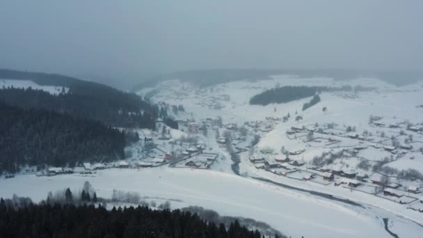 凍結した川のほとりの雪の中の村の空中風景 — ストック動画