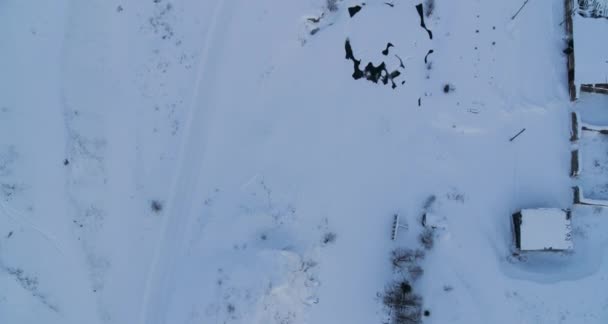 Vista aérea de uma aldeia na neve no inverno na margem de um rio congelado — Vídeo de Stock