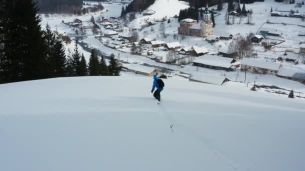 Widok z lotu ptaka na snowboard, który zjeżdża z góry na tle wioski — Wideo stockowe
