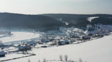 Kışın donmuş bir nehrin kıyısında ahşap evleri olan bir köyün hava manzarası.