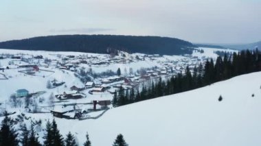 Kışın donmuş bir nehrin kıyısında ahşap evleri olan bir köyün hava manzarası.
