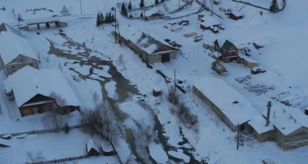 凍結した川のほとりで冬の雪の中の村の空中風景 — ストック動画